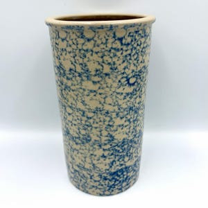 May include: Tall, cylindrical stoneware vase with a speckled blue and beige pattern. The vase has a slightly flared rim and a smooth, unglazed interior. A classic piece for home decor.