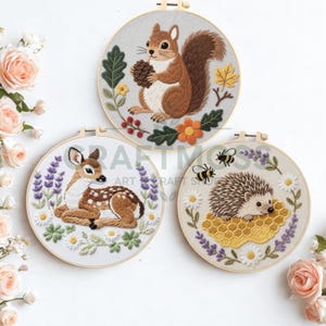 May include: Three embroidered hoops featuring woodland creatures. A squirrel holding a pinecone, a fawn resting in flowers, and a hedgehog on a honeycomb with bees. Each design is framed in a wooden hoop, showcasing detailed needlework.