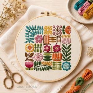 May include: A circular wooden embroidery hoop containing a white fabric panel with a multi-colored floral and bird pattern. The design features various embroidered flowers, leaves, and a central bird motif in shades of pink, yellow, orange, blue, and green.