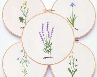 May include: Five embroidery hoops with floral designs. The designs include a yellow flower, a purple lavender, a blue flower, a bluebell, and a daisy. Each design is stitched on white fabric and set in a wooden hoop.