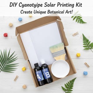 May include: DIY Cyanotype Solar Printing Kit in an open cardboard box. The kit includes bottles of chemicals, a paintbrush, a white ceramic bowl, and a stack of white paper. The text on the box reads: "Create Unique Botanical Art!"