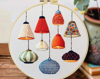 May include: Embroidered hoop art featuring eight colorful lampshades. The lampshades are in various shapes and colors, including red, orange, blue, and green. The artwork is set against a white background and framed in a wooden hoop.