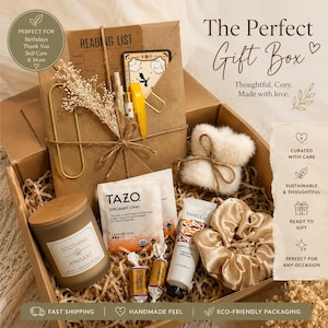 May include: A cardboard gift box containing a brown paper reading list folder, a Tazo organic chai tea bag, a vanilla hand cream tube, a gold-toned scrunchie, a small candle with a wooden lid, two small candies, and a white faux fur accessory.