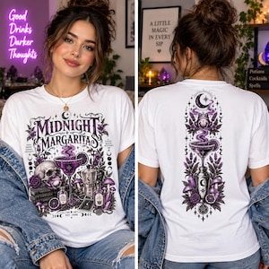 May include: A white t-shirt featuring a purple and black graphic design. The front displays the text Midnight Margaritas with a skull, a frog, a cocktail glass, and potion bottles. The back shows a vertical illustration of a frog, a cocktail glass, and a shaker surrounded by botanical elements and celestial symbols.