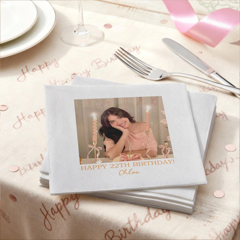 May include: A stack of white square napkins with a printed photo of a person and text that reads "HAPPY 22TH BIRTHDAY! Chloe". The napkins are on a table with a tablecloth that has the words "Happy Birthday" printed on it.