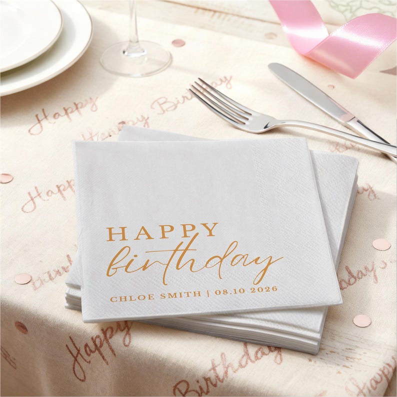 Peut inclure: Une pile de serviettes en papier blanches avec le texte dor&eacute; "HAPPY birthday" et le nom "CHLOE SMITH | 08.10 2026". Les serviettes sont sur une table avec une nappe "Happy Birthday", une fourchette, un couteau et un ruban rose.