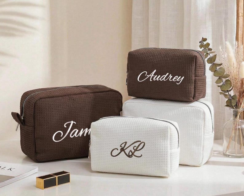 Pu&ograve; includere: Quattro trousse per cosmetici personalizzate in marrone e bianco. Le borse marroni hanno i nomi "Jam" e "Audrey" ricamati in corsivo bianco. Le borse bianche hanno le iniziali "KL" ricamate in corsivo nero. Tutte le borse hanno una trama a nido d'ape.