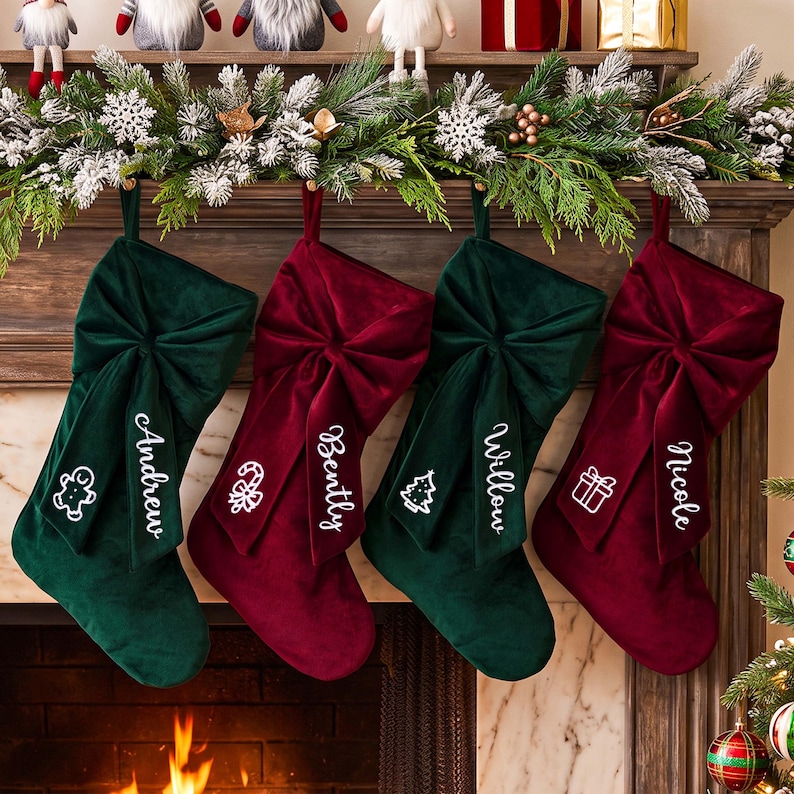 May include: Four velvet Christmas stockings in alternating dark green and deep red colours, each featuring a large fabric bow and a white embroidered name and holiday icon. The names Andrew, Bently, Willow, and Nicole are displayed.