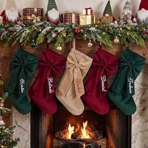 May include: Five velvet Christmas stockings hanging in a row, featuring two dark green, two deep red, and one beige stocking. Each stocking has a large decorative bow and is embroidered with a name: Kristin, Belinda, Rachel, Daniel, and Joshua.