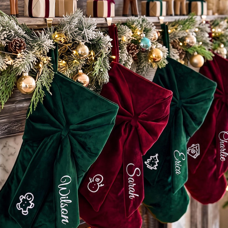 May include: A row of velvet Christmas stockings in deep green and burgundy, each featuring a large central bow and white embroidered names including Wilson, Sarah, and Erica, alongside small icons of a gingerbread man, snowman, and tree.