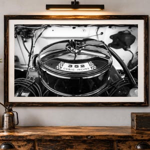 Könnte beinhalten: Ein schwarz-weiß gerahmtes Foto eines Luftfiltergehäuses für Oldtimer-Motoren. Der runde Metalldeckel zeigt ein Emblem mit einem Zielflaggenmuster und den Text 352 CUBIC INCHES, der in der Mitte des Gehäuses aufgedruckt ist.