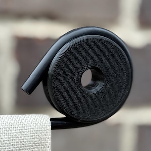 May include: Black metal towel rack with a unique spiral design. The rack holds a folded, light-colored towel. The background is a brick wall, providing a neutral backdrop for the bathroom accessory.