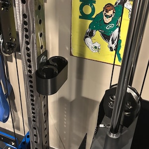 May include: A black weightlifting accessory attached to a silver metal weight machine. The accessory has two circular openings. A vintage Green Lantern sign is in the background.