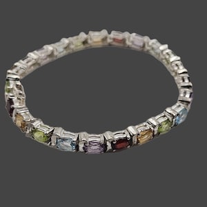 May include: A silver bracelet featuring a series of rectangular gemstones in various colors, including red, yellow, green, and blue. The bracelet is set against a dark gray background.