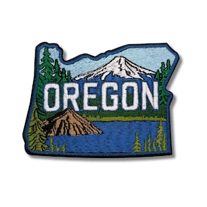 May include: Embroidered patch in the shape of Oregon, featuring a mountain, lake, and trees. The word "OREGON" is stitched in white block letters. The patch has a blue border and a white background.