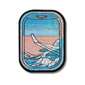Puede incluir: Parche bordado que representa un ala de avión vista a través de una ventana. El diseño incluye un cielo azul, un atardecer rosa y naranja y nubes blancas. El parche tiene un borde negro.