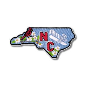 May include: Embroidered patch in the shape of North Carolina. Features a red cardinal perched on a flowering branch, the letters "NC" in red, and a mountain scene. The patch has a blue background and a black border.