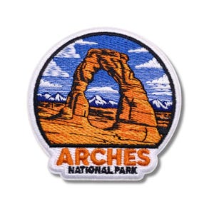 Könnte beinhalten: Runder, gestickter Aufnäher mit dem Delicate Arch im Arches National Park. Der Aufnäher hat einen weißen Rand, einen blauen Himmel und einen orangefarbenen Bogen. Der Text "ARCHES NATIONAL PARK" ist unten abgebildet.