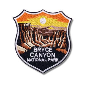 May include: Embroidered patch featuring a shield design with a landscape of Bryce Canyon National Park. The patch includes a sunset with a sun, canyon formations, and the text "BRYCE CANYON NATIONAL PARK" in white lettering.