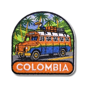 Puede incluir: Parche bordado con un autobús colorido con un tucán en la parte superior, sobre un fondo tropical de palmeras. La palabra "COLOMBIA" se muestra en una pancarta naranja en la parte inferior. El autobús es naranja, azul y amarillo.
