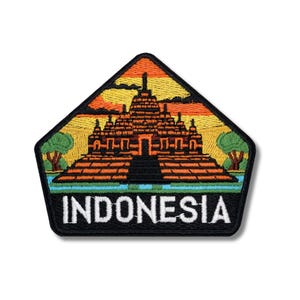 May include: Embroidered patch featuring the Borobudur temple in Indonesia. The patch has a black border and a pentagon shape. The temple is brown with a sunset background. The word "INDONESIA" is in white letters.