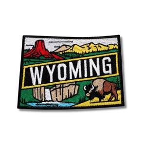 Op de afbeelding: Geborduurde patch met het woord "WYOMING" in witte blokletters op een zwarte en gouden achtergrond. De patch bevat een rode rotsformatie, bergen, een waterval en een bizon.
