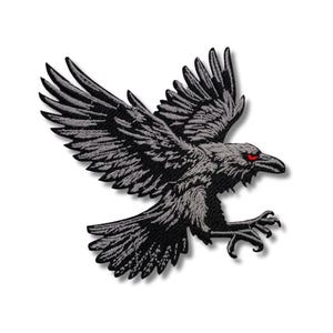 May include: Embroidered patch featuring a black raven in flight with outstretched wings. The raven has detailed feathering and piercing red eyes, set against a white background. The patch is designed with a shadow effect.