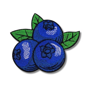 Może przedstawiać: Haftowana naszywka przedstawiająca trzy niebieskie jagody z białymi detalami i zielonymi liśćmi. Jagody mają teksturowany wygląd, a liście są jasnozielone.