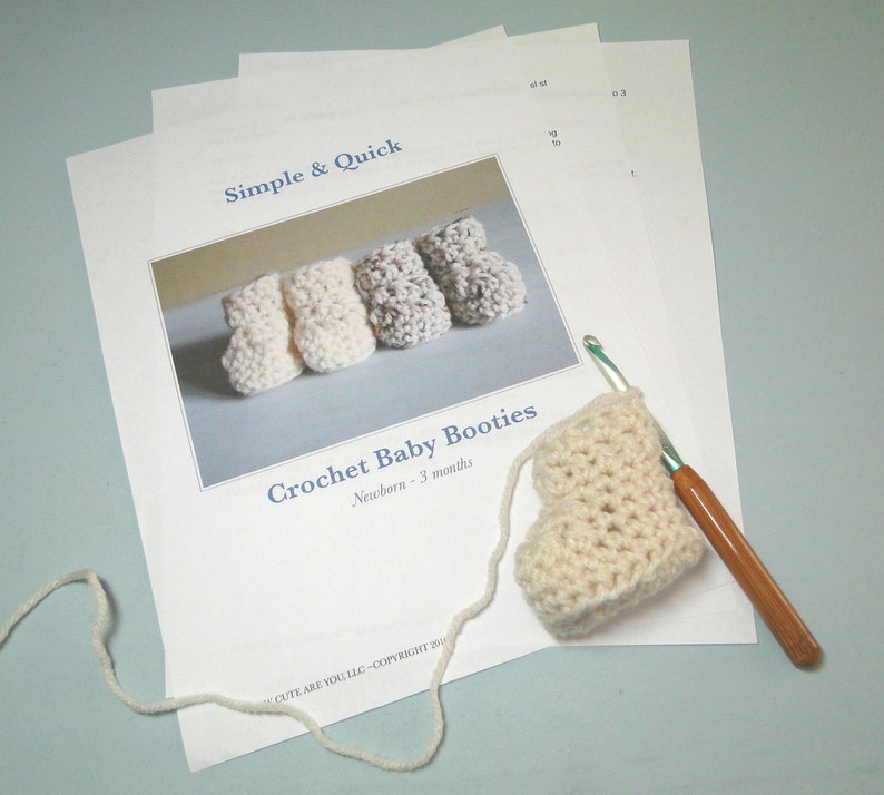 K&ouml;nnte beinhalten: Ein H&auml;kelmuster f&uuml;r Babyschuhe, mit einer Nahaufnahme eines geh&auml;kelten Sch&uuml;hchens und einer H&auml;kelnadel. Das Muster ist mit "Simple & Quick Crochet Baby Booties, Newborn - 3 months" betitelt.