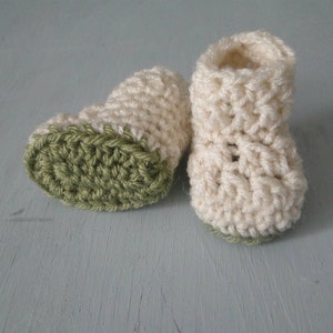 K&ouml;nnte beinhalten: Ein Paar geh&auml;kelte Babyschuhe mit einem wei&szlig;en Oberteil und einem gr&uuml;nen Unterteil.