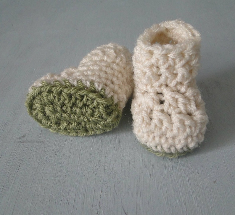 K&ouml;nnte beinhalten: Ein Paar geh&auml;kelte Babyschuhe mit einem wei&szlig;en Oberteil und einem gr&uuml;nen Unterteil.