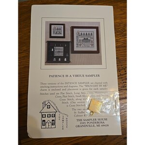 May include: A printed page featuring three framed cross-stitch samplers, with the text "PATIENCE IS A VIRTUE SAMPLER." The page includes instructions, diagrams, and a small gold-colored charm. The samplers depict houses and trees.