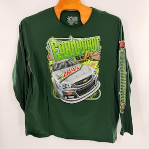 May include: Green long-sleeve shirt featuring a graphic of a race car with the text "Earnhardt Jr." and "Mountain Dew". The sleeve has the text "Earnhardt Jr." in green. The shirt is hanging on a wooden hanger.