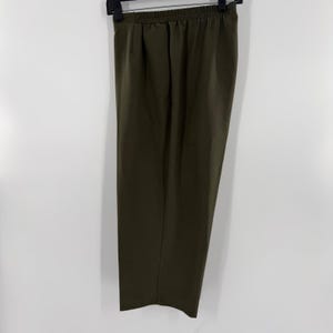 May include: Olive green pants with an elastic waistband, hanging on a black hanger. The pants have a straight leg design and are made of a smooth fabric. The pants are a solid color and appear to be new.