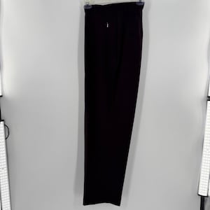 May include: Dark burgundy dress pants hanging on a white background. The pants have a straight leg design and a zipper closure. The fabric appears to be a smooth, solid color material. The pants are hanging from a black hanger.