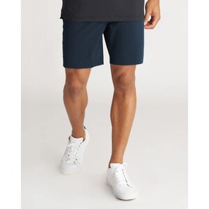 May include: Solid navy blue shorts featuring a clean, straight-leg cut that ends above the knee. The shorts are paired with a plain black t-shirt and white lace-up sneakers, creating a simple, functional outfit for casual or active wear.