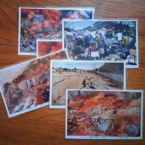May include: A collection of vintage postcards depicting scenes of destruction and aftermath. The images show buildings in flames, crowds of people, and damaged infrastructure. The postcards are arranged on a wooden surface.