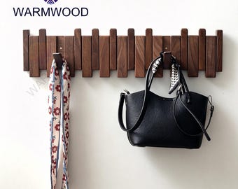Op de afbeelding: Een houten wandkapstok met meerdere haken. Een zwarte handtas en een sjaal met patroon hangen eraan. De merknaam "WARMWOOD" staat linksboven.