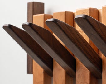 May include: A wall-mounted coat rack featuring a series of vertical wooden slats in alternating light and dark brown tones. Several dark brown wooden pegs extend outward at an upward angle from the base, providing multiple hooks for hanging items.