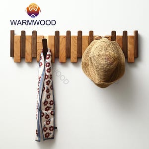 May include: A wooden wall-mounted coat rack with alternating light and dark wood slats. A straw hat and a floral scarf hang from the hooks. The brand name "WARMWOOD" is displayed in the upper left corner.