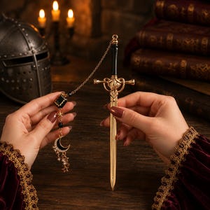 Può includere: Un apricarta color oro a forma di spada, con manico nero e elsa decorativa. Un ciondolo abbinato con un quadrato nero, stelle, una luna crescente e perline pendenti è attaccato da una catena. Lo sfondo include un elmo medievale e libri.