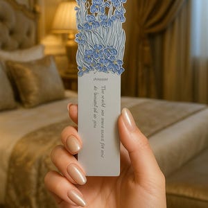 以下が含まれることがあります： 青いアヤメの花柄が特徴の長方形のブックマーク。ブックマークの上部には、花の詳しいイラストが描かれています。「thinasant」という文字と引用句がブックマークに印刷されています。