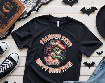 May include: Black t-shirt with a cartoon illustration of a female Frankenstein's monster in a pink dress. The text "Franken Fest! Happy Haunting!" is printed around the image. Black Converse sneakers and Halloween decorations are in the background.
