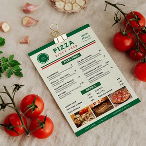 May include: A pizza menu with a green and white design, featuring the text "PIZZA SINCE 2020". Fresh tomatoes, garlic cloves, and parsley sprigs are arranged around the menu. The menu includes pizza and drink options.