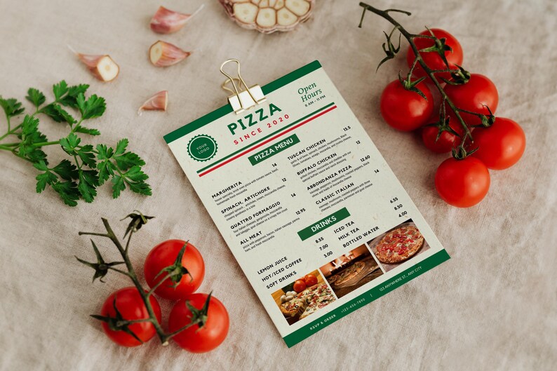 May include: A pizza menu with a green and white design, featuring the text "PIZZA SINCE 2020". Fresh tomatoes, garlic cloves, and parsley sprigs are arranged around the menu. The menu includes pizza and drink options.