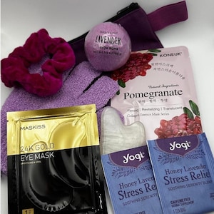 May include: A selection of self-care products, featuring a lavender bath bomb, eye masks, a face mask, a gua sha tool, a scrunchie, and two Yogi Honey Lavender Stress Relief tea bags. The items are in shades of purple, gold, and white.