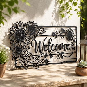 Könnte beinhalten: Ein schwarzes Metall-Wandschild mit dem Wort Welcome in Schreibschrift, verziert mit komplexen Sonnenblumen- und Blattausschnitten auf der linken Seite und kleineren floralen Akzenten auf der rechten Seite, alles in einem rechteckigen Rahmen.
