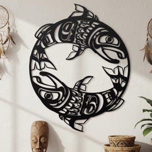 Peut inclure: Décoration murale en métal noir représentant deux poissons stylisés dans un cercle. Les poissons sont représentés dans un style d'art tribal amérindien, avec des motifs détaillés. L'œuvre est fixée sur un mur blanc.