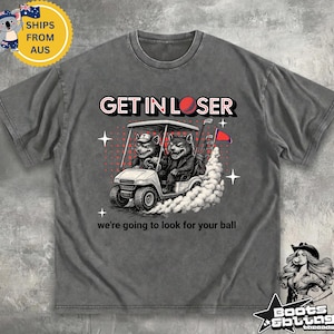 May include: Gray t-shirt with a graphic of two cartoon wolves in a golf cart, the text "GET IN LOSER" and "we're going to look for your ball". The design includes a golf ball and clubs.