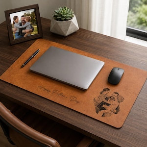 Könnte beinhalten: Eine braune Leder-Schreibtischunterlage mit dem Text "Happy Father's Day" und einem Familienporträt. Ein Laptop, eine Maus und ein Stift befinden sich auf der Unterlage. Ein gerahmtes Foto und eine Sukkulente in einem geometrischen Topf befinden sich ebenfalls auf dem Schreibtisch.